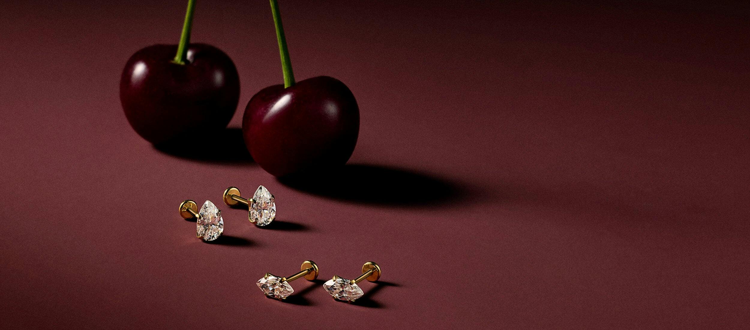 Marquise and Pear Nap Earrings on a dark red background with cherries.